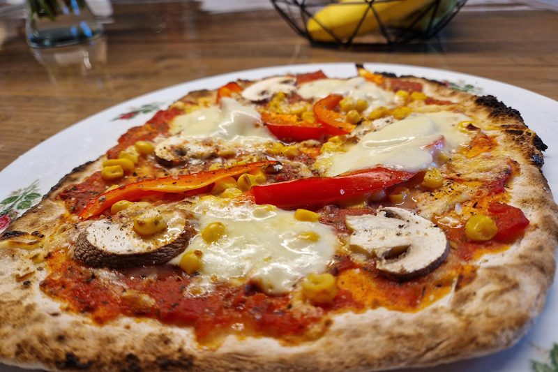 Fertig gebackene Pizza mit Champignons, Paprika und Mais, der Rand ist dunkel aufgegangen