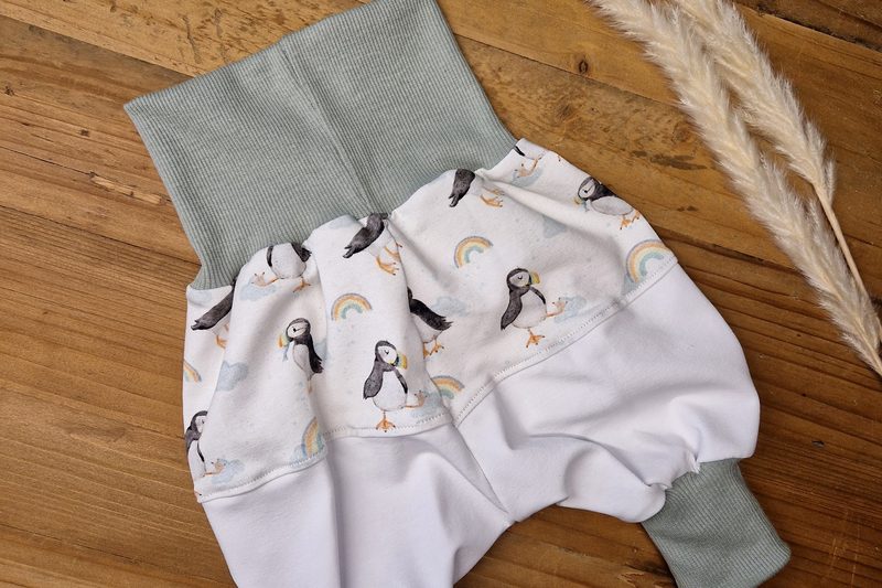 Babyhose mit Papageitauchern und Regenbogen, mintgrüne Bündchen, auf Holzdielen neben einer Pampasgras-Rispe