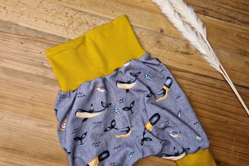 Babyhose mit Walen und Booten auf graublauem Grund, senfgelbe Bündchen, auf Holzdielen