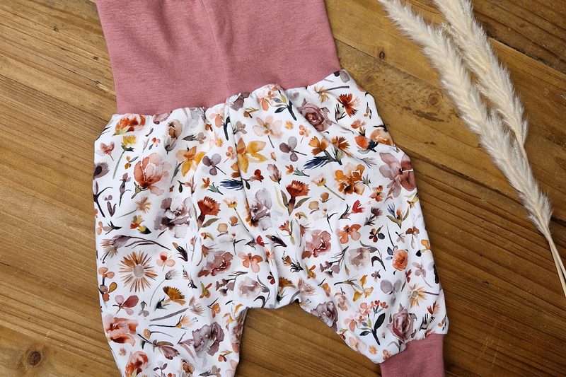 Babyhose mit gemaltem Blumendruck in Ocker und Rosé, altrosa Bündchen, auf Holzdielen