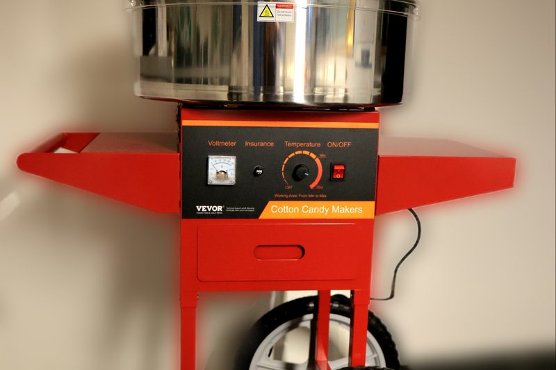 Roter Rollwagen mit Edelstahlschüssel unter einer klaren Haube, darunter Voltmeter, Temperaturregler und Kippschalter